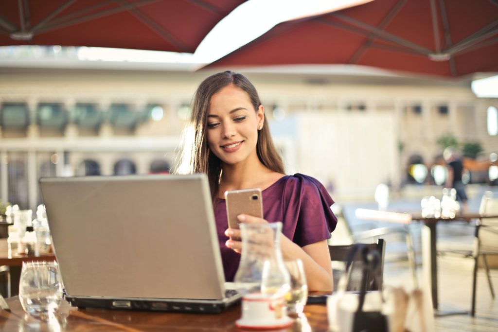 Conventional loans. A young woman smiles at her phone while working on a laptop, symbolizing the achievement of good news found